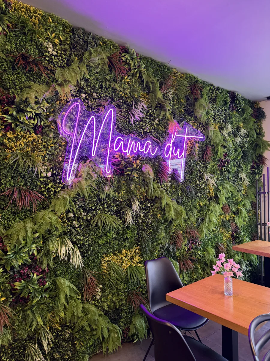 Pflanzenwand mit Neon-Schriftzug im Café mama dut in Bielefeld